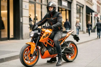 Jeune motard en équipement noir et orange assis sur une KTM Duke 125 orange garée en ville
