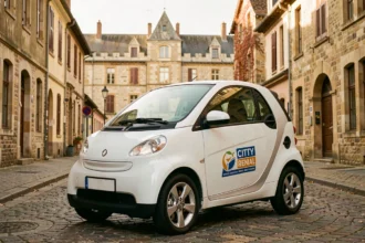 Petite voiture sans permis blanche garée dans une rue pavée de Dijon avec le Palais des Ducs en arrière-plan