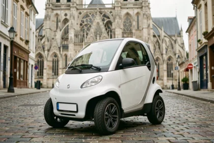 Voiture sans permis blanche garée dans une rue pavée de Rouen avec la cathédrale en arrière-plan