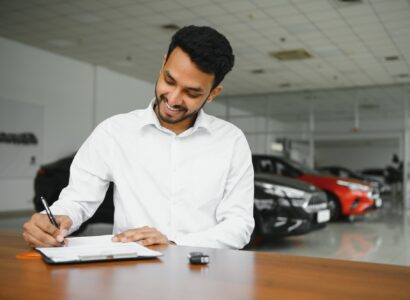 young indian man signing documents at car dealership