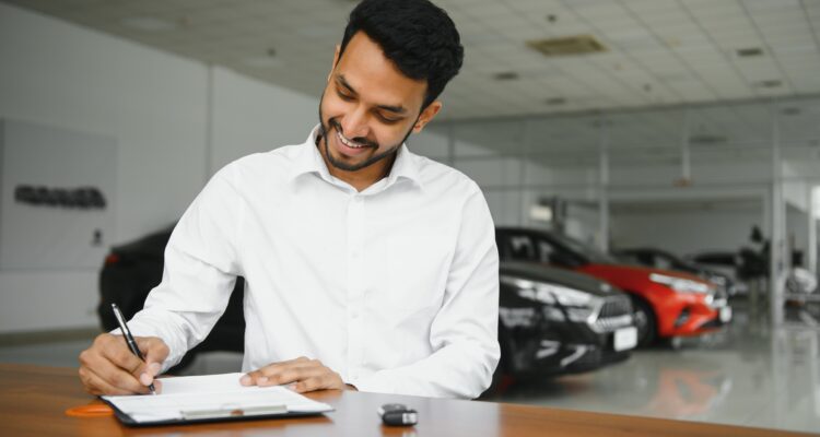 young indian man signing documents at car dealership